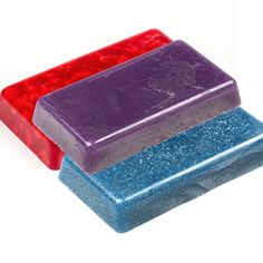 three different colored soap bars sitting next to each other on a white surface with red and blue flecks