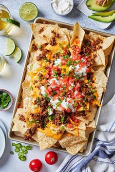 a tray filled with nachos and salsa on top of a table next to sliced avocados