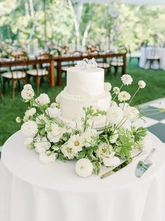 a white wedding cake sitting on top of a table covered in flowers and greenery