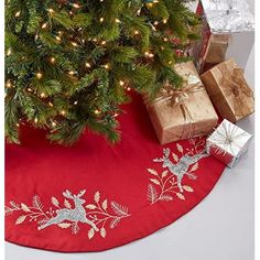 a christmas tree skirt with presents under it on a red tablecloth next to a small christmas tree