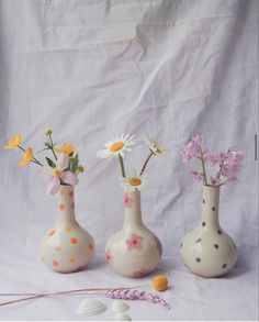 three vases with flowers in them on a white background