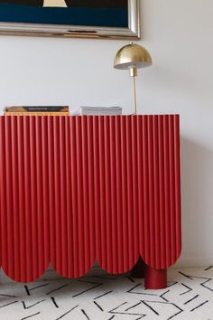 a red cabinet in the corner of a room with a painting on the wall behind it