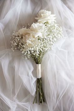 a bouquet of white flowers sitting on top of a white cloth covered bed sheet with tulle