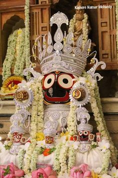 an idol is displayed in front of some flowers and garlands on the wall behind it