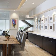 a dining room table with chairs and pictures on the wall behind it in an open area