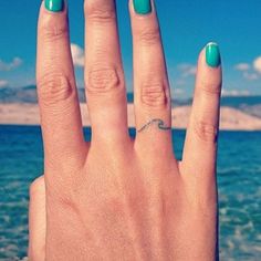 a woman's hand with green nail polish on it and the ocean in the background