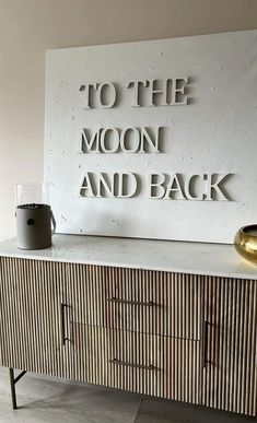 a sideboard with the words to the moon and back on it next to a vase