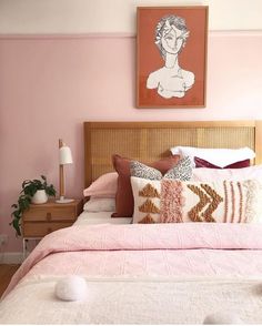 a bedroom with pink walls and white bedding, artwork on the wall above it