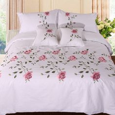 a bed with white sheets and pink flowers on the comforter, along with two pillows