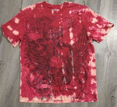 a red tie - dye shirt with skulls and wings on it sitting on a wooden floor