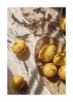 some lemons are sitting in a bowl on top of a white cloth tablecloth