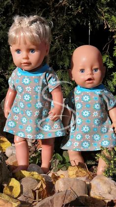 two dolls standing next to each other in front of some rocks and trees with leaves