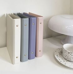 three binders are next to a cup and saucer on a white countertop