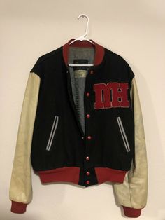 a black and red jacket hanging up on a white wall with the letter m in it