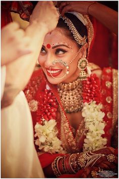 a woman in a red and gold bridal outfit with jewelry on her face, smiling at the camera