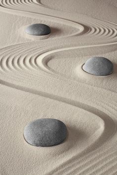 four rocks sitting on top of sand in the shape of spirals and circles with wavy lines