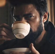 a man drinking from a coffee cup while holding a saucer in his right hand