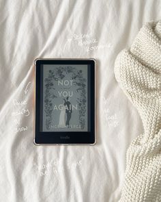 a kindle sitting on top of a white blanket next to a book titled not you again