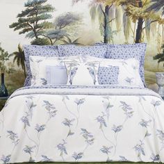 a bed with blue and white comforters in front of a wallpapered mural