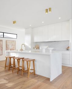 a white kitchen with three stools in front of the island and an open floor plan