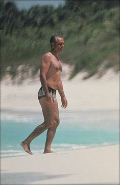 an older man walking on the beach with his surfboard