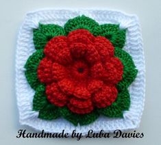 a crocheted square with a red flower on top and green leaves in the middle