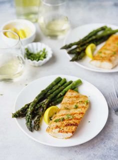 two white plates topped with fish and asparagus