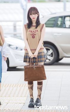 a young woman is standing on the sidewalk with her hand in her pocket and holding a brown purse