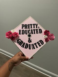 a person holding up a pink and black graduation cap with roses on it that says pretty, educated & graduated