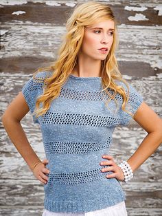 a woman standing in front of a wooden wall wearing a blue sweater and white shorts