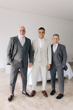 three men in suits standing next to each other on a carpeted floor with white sheets