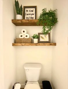 a white toilet sitting in a bathroom next to a wooden shelf filled with towels and plants