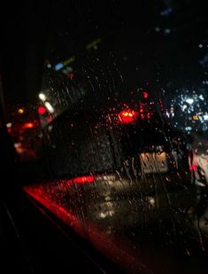 the back window of a car at night with rain on it and street lights in the background