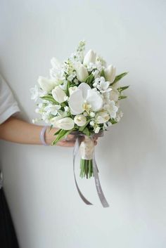 a bouquet of white flowers is held by a woman's hand against a wall