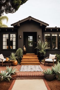 a black house with white chairs and plants in front of the entrance to the house