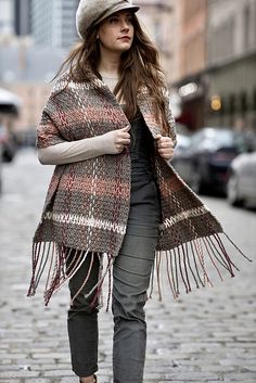 a woman is walking down the street wearing a plaid poncho and fringe jacket