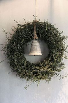 a bell hanging from the side of a wall next to a wreath with branches on it