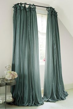 the curtains are hanging in front of the window and there is a vase with flowers on it