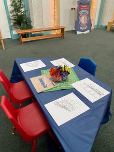 the table is covered with blue cloth and red plastic chairs are next to each other