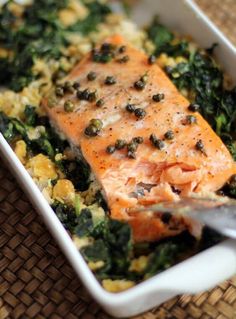 salmon and greens in a white dish with a spoon on the side, ready to be eaten