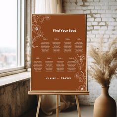 a seating chart on an easel next to a vase with dried grass in it