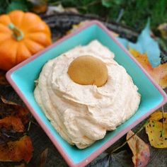 a small blue plate topped with whipped cream next to some pumpkins and autumn leaves