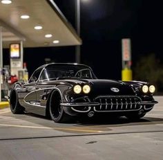 an old black car parked in front of a gas station at night with lights on