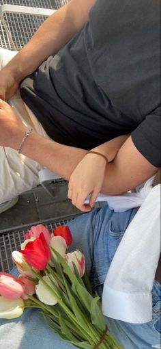 two people sitting next to each other with flowers in front of them on the ground