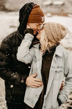 a man and woman kissing in the snow while wearing winter clothes, hats and scarves