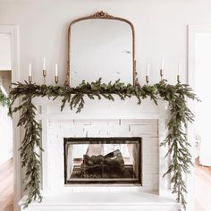 a white fireplace decorated with greenery and candles