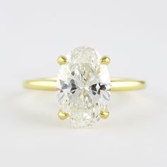 an oval cut diamond ring with three clawed shans in yellow gold, on a white background