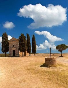 an old church in the middle of a field with trees on either side and a blue sky with white clouds