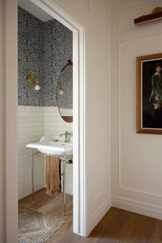 a white sink sitting under a mirror in a bathroom next to a painting on the wall