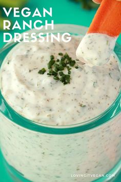 a carrot being dipped with ranch dressing in a glass bowl on a green tablecloth